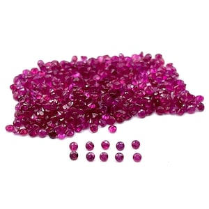 Peut inclure: Un grand tas de petites pierres précieuses de rubis rondes et rouges. Les rubis sont facetés et ont un éclat brillant. Il y a aussi quelques rubis disposés en rangée sous la pile.
