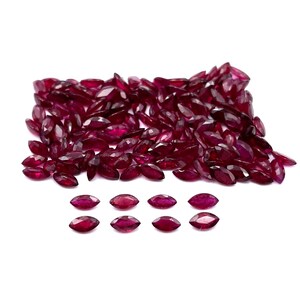 May include: A large pile of loose, red, marquise-shaped gemstones. There are also eight smaller, red, marquise-shaped gemstones arranged in two rows of four.