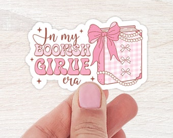 May include: Pink and white sticker with the text "In my bookish girlie era" and a pink book with a bow and pearl necklace.