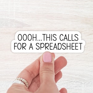May include: A white sticker with black text that reads "OOOH...THIS CALLS FOR A SPREADSHEET". The sticker is held by a hand with pink nail polish and rings.
