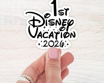 May include: A white sticker with black text that reads "1st Disney Vacation 2026". The word "Disney" is in a stylized font. The sticker is held by a hand with pink nail polish.