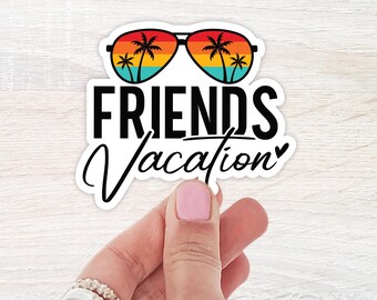 May include: A white sticker with the words "FRIENDS Vacation" in black script. The sticker features a pair of sunglasses with a sunset design and palm trees reflected in the lenses. The sticker is held by a person.