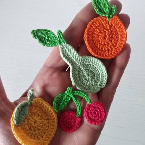 Può includere: Applicazioni di frutta all'uncinetto in vari colori, tra cui arancione, giallo, verde e rosso. Le applicazioni hanno la forma di arance, pere e ciliegie.