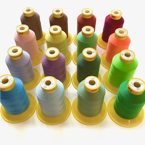 May include: Assortment of 18 spools of Gutermann thread in various colours, including green, blue, pink, purple, orange, yellow, and brown. Each spool is labelled with the Gutermann brand name.