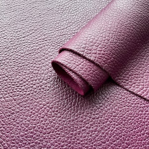 May include: Close-up of a deep purple leather with a textured, pebbled surface. The leather is folded over on itself, showing the soft, supple texture.