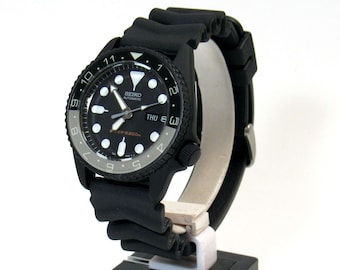 May include: A black Seiko automatic wristwatch with a black rubber band. The watch face has white markings and a date window that reads "THU 8".