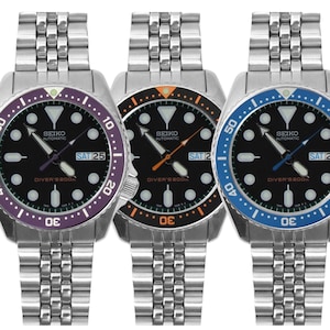 May include: Three Seiko automatic diver's 200m watches with stainless steel link bracelets and black dials. Each watch features a day-date window and a rotating bezel in purple, orange, or blue, with matching colored second hands and markers.