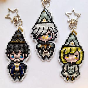 May include: Three handmade pixel art keychains featuring anime-style characters. Each keychain is a different character with unique hair and clothing. The keychains are attached to silver star-shaped clasps. Yellow flowers are in the background.