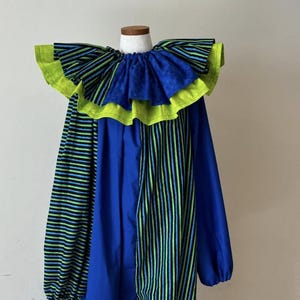 May include: A blue clown costume with a large ruffled collar. The collar is blue with a neon green trim. The sleeves and front panel feature vertical stripes of blue and neon green. The text "DesignsbySarah SewBright" is visible.