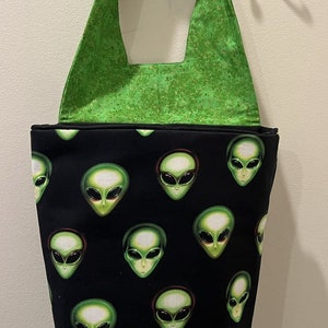 May include: A black reusable tote bag with a green strap. The bag has a repeating pattern of green alien faces.