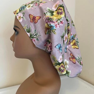 May include: A purple scrub hat with a floral print featuring butterflies and flowers. The hat is made of soft, comfortable fabric and is perfect for nurses, doctors, and other healthcare professionals.