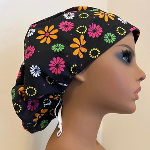 May include: Black scrub cap with a colorful floral pattern featuring pink, orange, green, and white flowers on a black background. The cap has a drawstring for adjusting the fit.