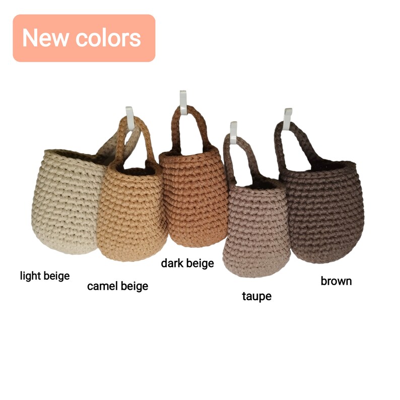 May include: Five crocheted hanging baskets in different shades of beige and brown. The baskets are labeled "light beige", "camel beige", "dark beige", "taupe", and "brown".