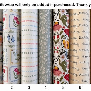 May include: Seven rolls of gift wrapping paper arranged side by side. Patterns include colorful wildflowers, framed botanical illustrations, pastel dots, a gray floral print, a vibrant garden motif, cream paper with Happy Birthday text, and plain brown.