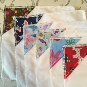 May include: Five white fabric squares with different patterned fabric triangles sewn into the corners. The patterns include brown with hearts, blue with umbrellas, blue with butterflies, blue with candy, and red with polka dots.