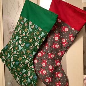 May include: Two Christmas stockings hanging side by side. The left stocking has a green cuff and a green body patterned with gingerbread men, candy canes, snowmen, and trees. The right stocking has a red cuff and a grey body with Santa Claus.