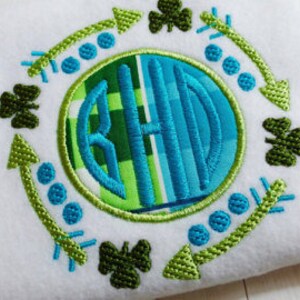 Peut inclure: Un motif de broderie de monogramme vert et bleu avec des trèfles et des flèches autour du cercle. Le monogramme est les lettres "BHD" en police blanche.
