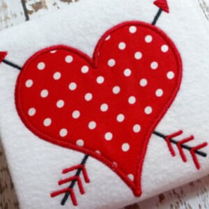 May include: Red heart with white polka dots and two red arrows crossing through it. The heart is outlined in white.