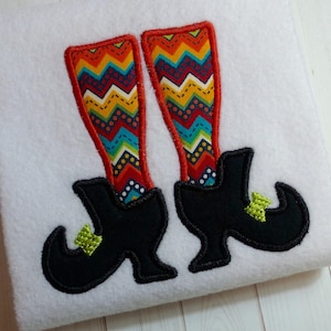 Puede incluir: Un par de botas de bruja negras con hebillas verdes y calcetines con estampado de chevron de colores.