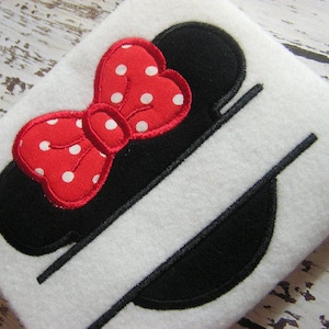 May include: A black and white split monogram design featuring a red bow with white polka dots. The bow is in the shape of Minnie Mouse's ears.