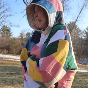 May include: A quilted hooded jacket with a patchwork design. The jacket features a variety of colors, including pink, yellow, green, blue, and white. The hood is also patchwork, and the jacket appears to be warm and cozy.