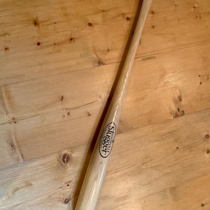 Puede incluir: Un bast&oacute;n de madera de color claro fabricado a partir de un bate de b&eacute;isbol, con un mango curvado en la parte superior y una punta de goma negra en la base. El cuerpo muestra el logotipo negro de Louisville Slugger impreso en la madera.