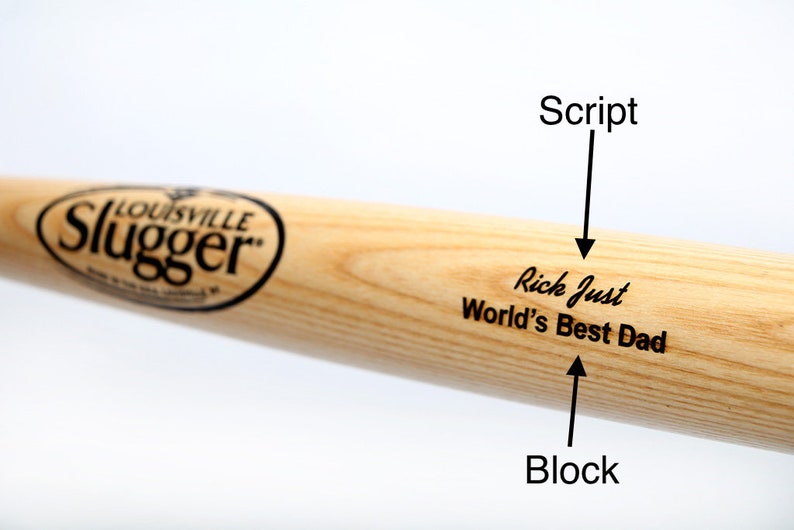 Puede incluir: Un bate de b&eacute;isbol de madera clara con el logotipo negro de Louisville Slugger. El bate est&aacute; grabado con el texto Rick Just en fuente cursiva y World's Best Dad en fuente de bloque, con flechas que se&ntilde;alan cada estilo de texto.