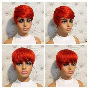 May include: A vibrant, short, red wig with a layered, side-swept bang. The wig is styled on a mannequin head, paired with large silver hoop earrings and a white top. The background is a tufted, white upholstered surface.