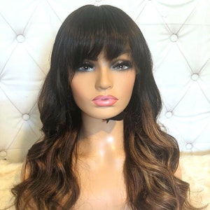 Może przedstawiać: Długa, falująca peruka w kolorze brązowym z blond pasemkami i grzywką.