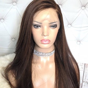 May include: A long, straight, dark brown human hair wig with a lace front. The wig is styled with a side part and falls to the shoulders.