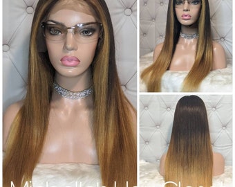 May include: A long, straight, ombre human hair wig with dark roots that gradually lighten to a light blonde at the ends. The wig is styled with a middle part and is worn on a mannequin head. The mannequin is wearing glasses.