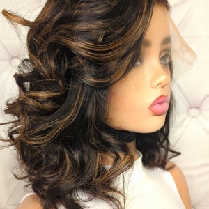 Może przedstawiać: Krótkie, falowane, brązowe peruka z blond pasemkami. Peruka jest ułożona z przedziałkiem z boku i ma naturalnie wyglądającą linię włosów.