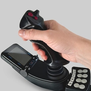 May include: A black flight simulator joystick controller featuring a contoured grip with two red top buttons, a small integrated digital display screen, and a side panel with four circular grey buttons and additional small white icon indicators.