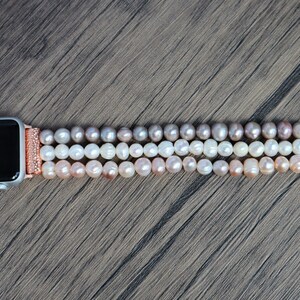 Puede incluir: Una pulsera de Apple Watch de oro rosa con un dise&ntilde;o de perlas de tres hilos. Las perlas son un degradado de rosa, blanco y crema.
