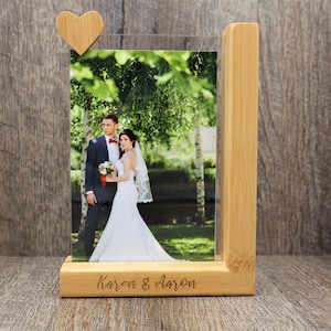 May include: A wooden photo frame with a picture of a couple on their wedding day. The frame is made of light-colored wood and has a small wooden heart attached to the top. The names "Karen & Aaron" are engraved on the base.