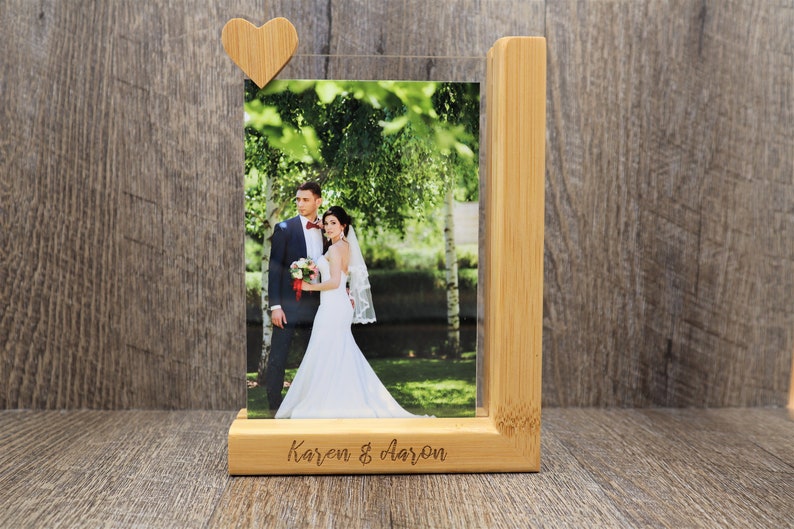 May include: A wooden photo frame with a picture of a couple on their wedding day. The frame is made of light-colored wood and has a small wooden heart attached to the top. The names "Karen & Aaron" are engraved on the base.