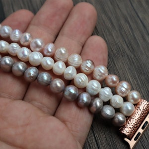 Puede incluir: Un brazalete de perlas de tres hilos con un adaptador de banda de Apple Watch de oro rosa. Las perlas son en tonos de blanco, rosa y gris.