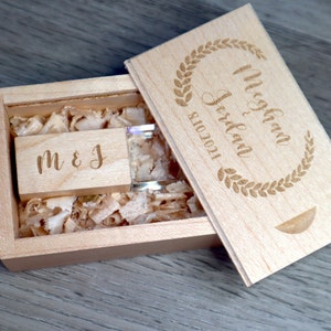 K&ouml;nnte beinhalten: Ein h&ouml;lzernes USB-Flash-Laufwerk und Box-Set. Der Deckel der Box ist mit den Namen "Meghan & Jordan" und dem Datum "8.10.2021" in einem Lorbeerkranz graviert. Das USB-Laufwerk ist mit den Initialen "M & J" graviert. Die Box ist mit Holzsp&auml;nen gef&uuml;llt.
