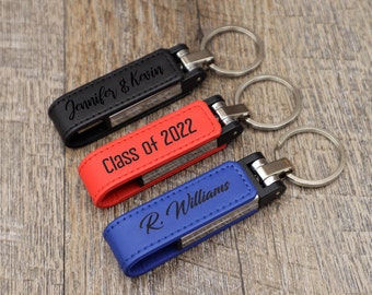 Puede incluir: Tres llaveros de cuero personalizados con anillos de metal. El llavero de la izquierda es negro y dice "Jennifer & Kevin". El llavero del medio es rojo y dice "Class of 2022". El llavero de la derecha es azul y dice "R. Williams".