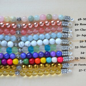 May include: A close-up of ten rows of colorful gemstone bracelets with silver clasps. The bracelets are arranged in a horizontal line from top to bottom. The bracelets are made of various gemstones, including morganite, rose hematite, cherry quartz, aquamarine, howlite, matte mix aqua, sugilite, mix color howlite, faceted gold hematite, and clear citrine.