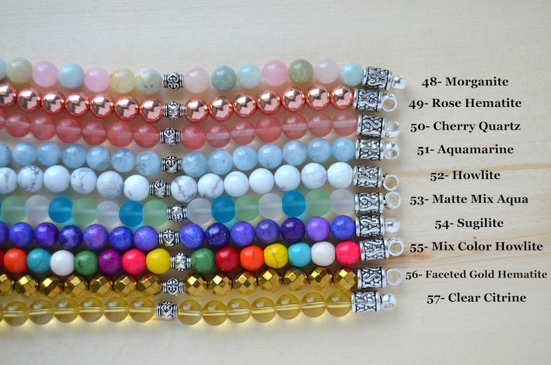 May include: A close-up of ten rows of colorful gemstone bracelets with silver clasps. The bracelets are arranged in a horizontal line from top to bottom. The bracelets are made of various gemstones, including morganite, rose hematite, cherry quartz, aquamarine, howlite, matte mix aqua, sugilite, mix color howlite, faceted gold hematite, and clear citrine.