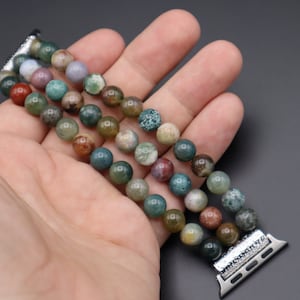 Puede incluir: Un brazalete de m&uacute;ltiples hilos hecho de cuentas de &aacute;gata verde, marr&oacute;n y roja. El brazalete est&aacute; dise&ntilde;ado para adaptarse a un Apple Watch y tiene un cierre de metal plateado.