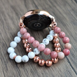 May include: Three beaded bracelets in rose gold, white, and pink. The bracelets are layered on top of each other and are attached to a rose gold watch band.