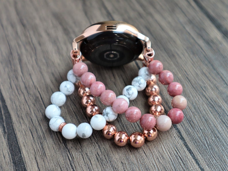 May include: Three beaded bracelets in rose gold, white, and pink. The bracelets are layered on top of each other and are attached to a rose gold watch band.