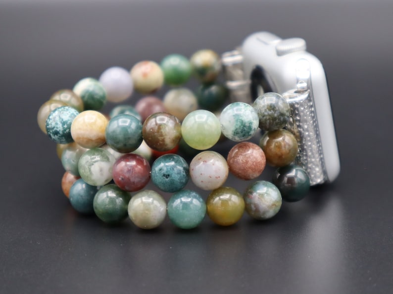 Puede incluir: Una pulsera de reloj de cuentas de &aacute;gata multicolor para un Apple Watch. La pulsera est&aacute; hecha de m&uacute;ltiples hilos de cuentas en tonos de verde, marr&oacute;n y blanco.