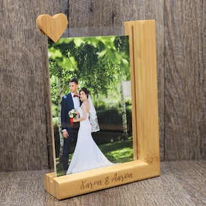 May include: A wooden photo frame with a heart-shaped clip holding a photograph of a couple. The frame is made of light-colored wood and has the names "Karen & Aaron" engraved on the base. The photo shows a bride and groom.