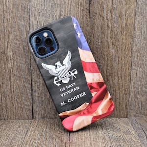 May include: A black phone case with a faded American flag design. The case features a white US Navy Veteran emblem with the words "US Navy Veteran M. Cooper".