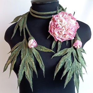 以下が含まれることがあります： 大きなピンクの牡丹と小さなピンクのつぼみが2つ付いた、フェルトの花のネックレス。ネックレスは緑の葉と茎で作られています。