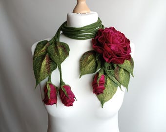 May include: A handcrafted felted rose scarf in shades of green and burgundy. The scarf features a green, coiled neckpiece, with felted leaves and three burgundy rose buds. A large burgundy rose is attached to the scarf. The scarf is displayed on a white mannequin.