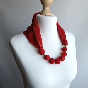 Könnte beinhalten: Eine rote Filzkette mit großen, runden Perlen. Die Kette wird auf einer weißen Schaufensterpuppe präsentiert.